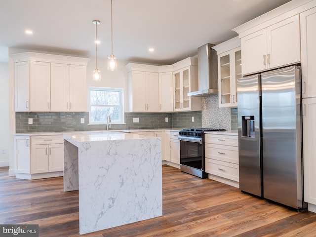 kitchen featuring a sink, wall chimney range hood, wood finished floors, and stainless steel appliances