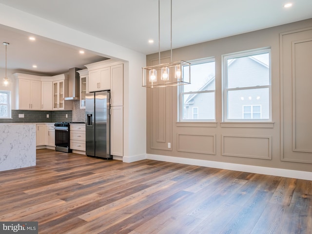 kitchen with tasteful backsplash, wall chimney range hood, dark wood-style floors, stainless steel fridge, and range