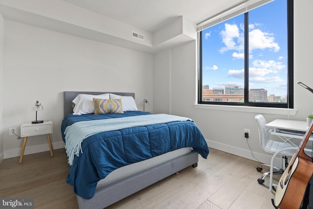 bedroom with a view of city, wood finished floors, visible vents, and baseboards