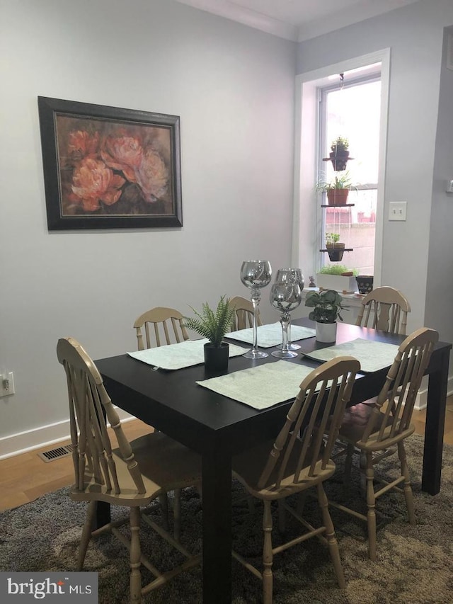 dining room featuring visible vents, baseboards, wood finished floors, and ornamental molding