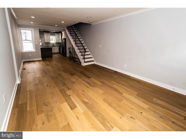 unfurnished living room with stairs, hardwood / wood-style flooring, crown molding, and baseboards