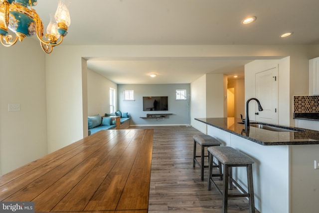 kitchen with white cabinetry, dark stone counters, dark wood-style flooring, a sink, and a kitchen bar