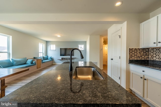 kitchen featuring an island with sink, a sink, open floor plan, white cabinets, and decorative backsplash