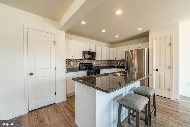 kitchen featuring a sink, black appliances, a breakfast bar, and light wood finished floors