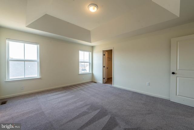 carpeted spare room featuring baseboards and a raised ceiling