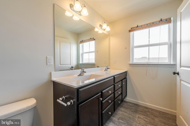 bathroom featuring toilet, a sink, wood finished floors, double vanity, and baseboards