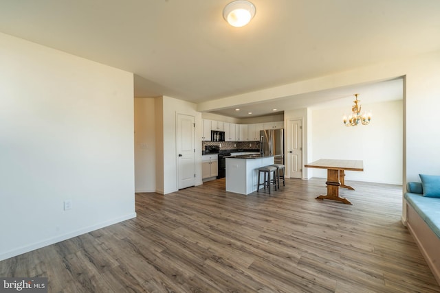 kitchen with tasteful backsplash, dark countertops, a kitchen breakfast bar, an inviting chandelier, and black appliances