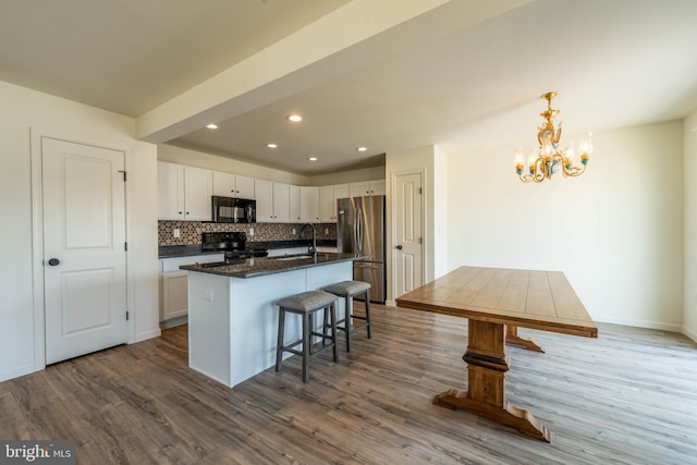 kitchen with dark wood-type flooring, black appliances, white cabinets, and an island with sink