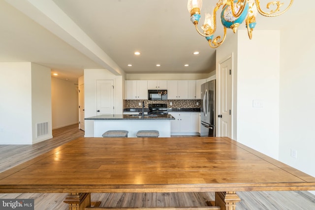 kitchen with visible vents, an island with sink, backsplash, freestanding refrigerator, and black microwave