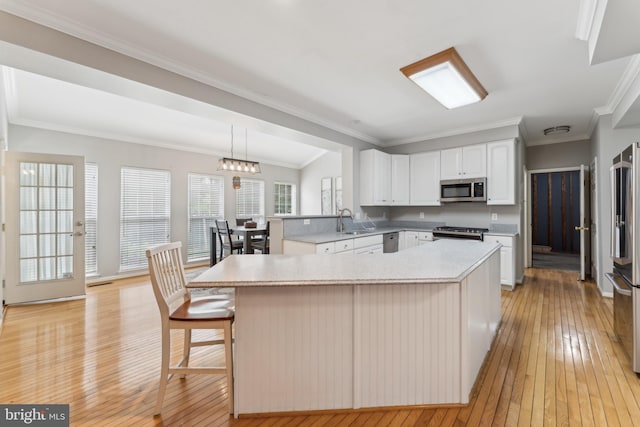 kitchen with stainless steel appliances, ornamental molding, light wood finished floors, light countertops, and white cabinets