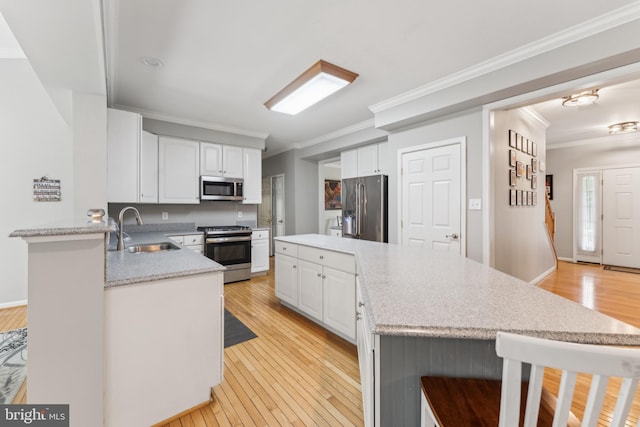 kitchen with light wood finished floors, a center island, a sink, stainless steel appliances, and ornamental molding