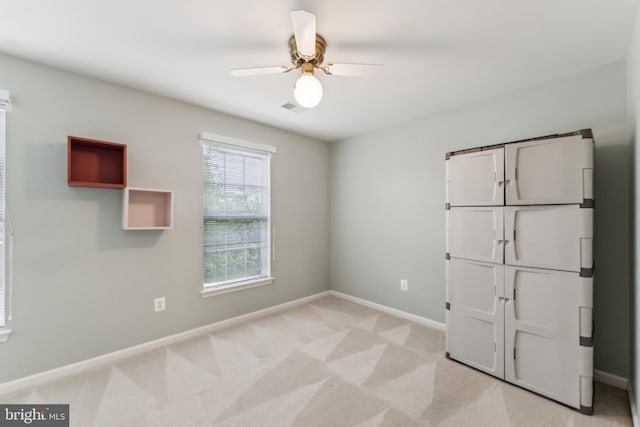 unfurnished room featuring baseboards, visible vents, a ceiling fan, and light colored carpet