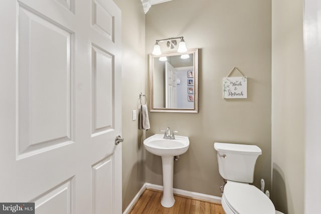 half bath with wood finished floors, baseboards, toilet, and a sink