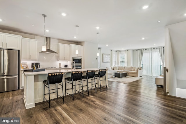 kitchen with wall chimney range hood, freestanding refrigerator, dark wood-style floors, a large island with sink, and built in microwave