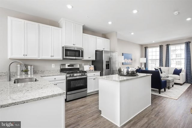 kitchen featuring a center island, appliances with stainless steel finishes, wood finished floors, white cabinetry, and a sink