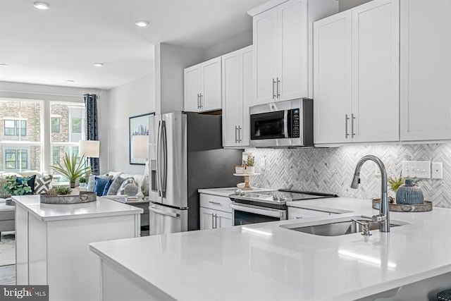 kitchen with a sink, open floor plan, a peninsula, appliances with stainless steel finishes, and light countertops