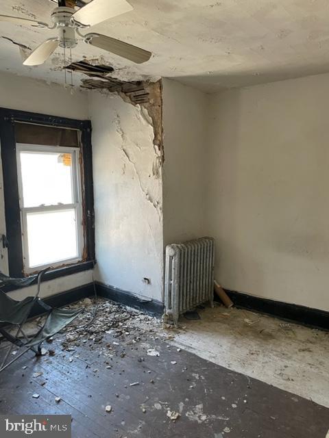 spare room featuring ceiling fan, radiator, and baseboards