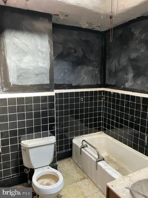 bathroom with tile walls, toilet, a bath, and a textured ceiling