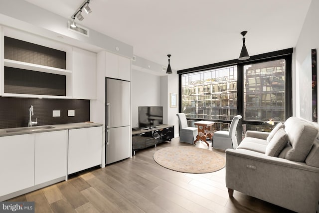 living area featuring track lighting, floor to ceiling windows, visible vents, and light wood finished floors