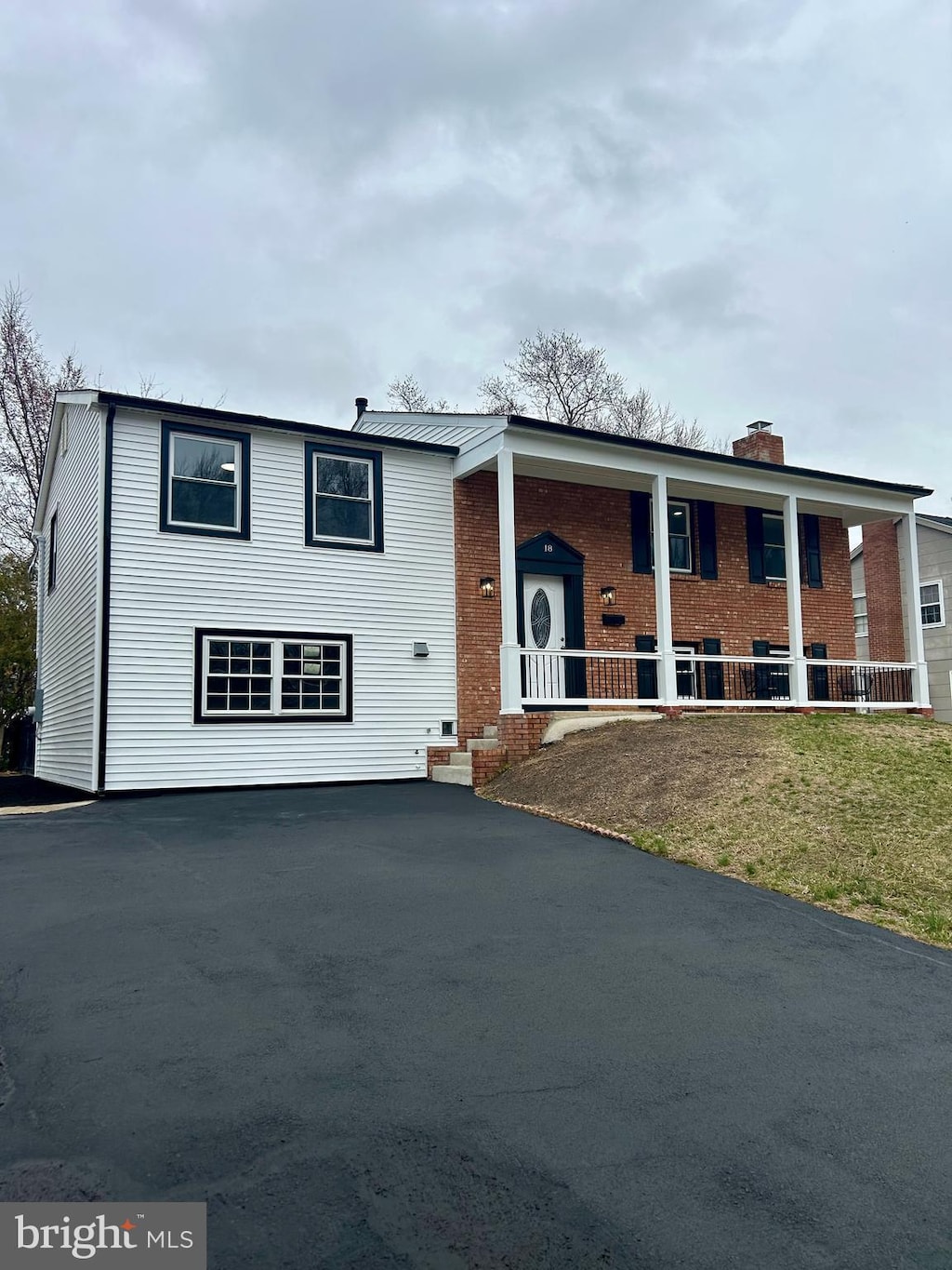 raised ranch with brick siding, covered porch, a chimney, and a front yard