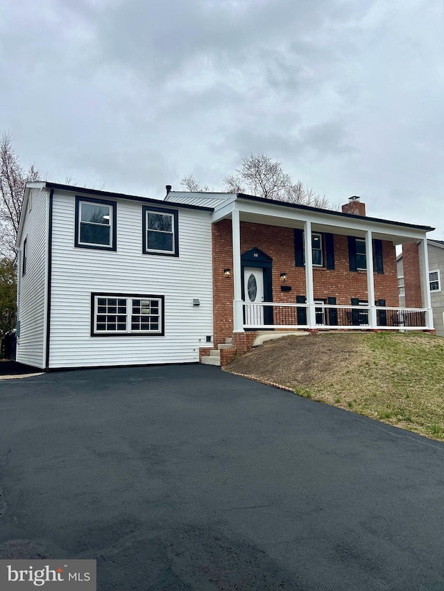 raised ranch with brick siding, covered porch, a chimney, and a front yard