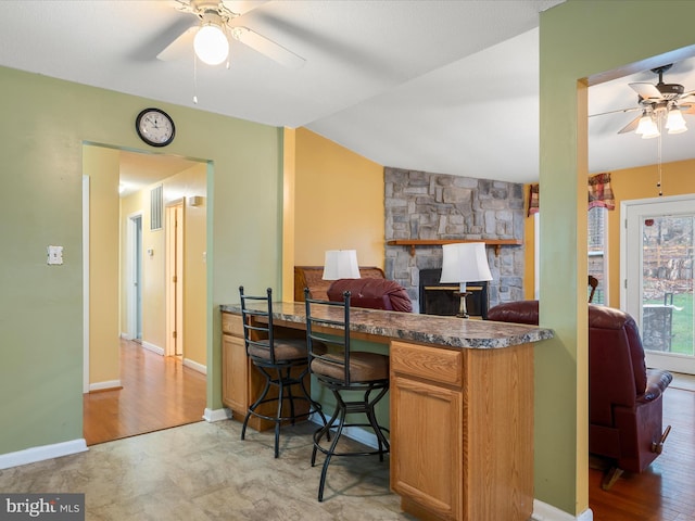 kitchen with a peninsula, a ceiling fan, a stone fireplace, open floor plan, and baseboards