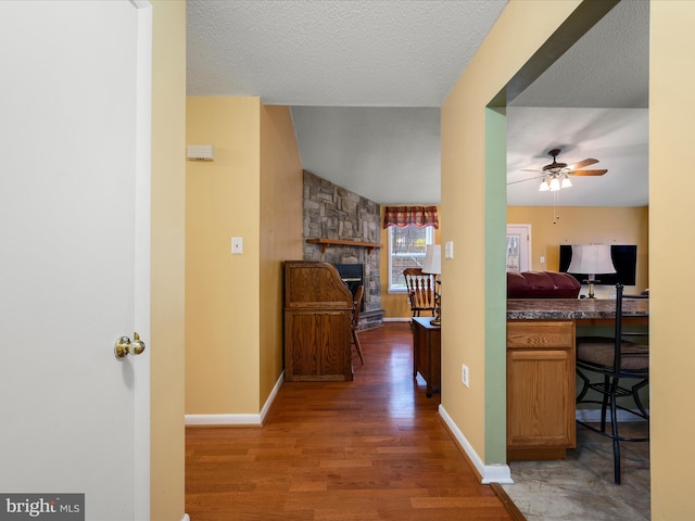 hall featuring lofted ceiling, baseboards, a textured ceiling, and wood finished floors