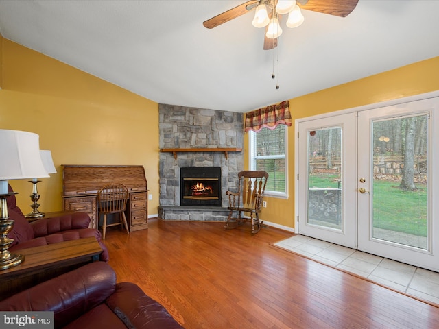 living area featuring lofted ceiling, ceiling fan, a stone fireplace, and wood finished floors