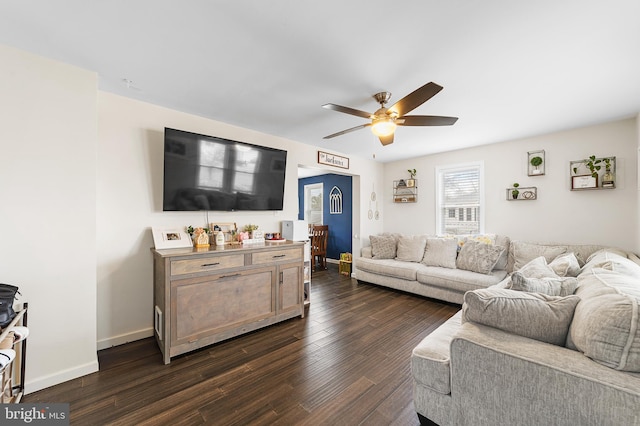 living area with baseboards, a ceiling fan, and dark wood-style flooring