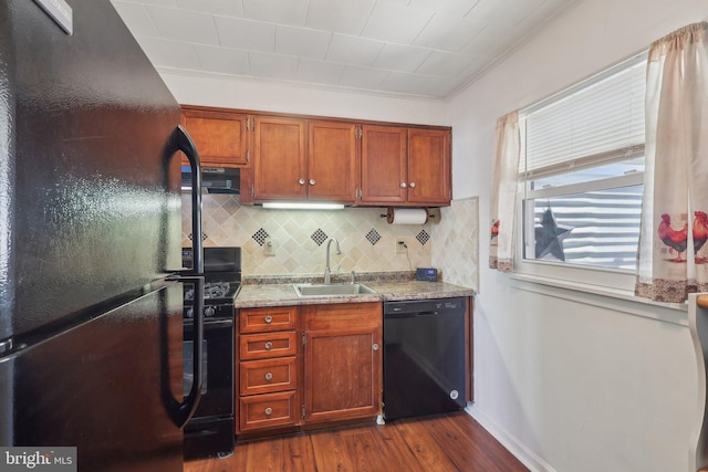 kitchen featuring exhaust hood, decorative backsplash, dark wood finished floors, a sink, and black appliances