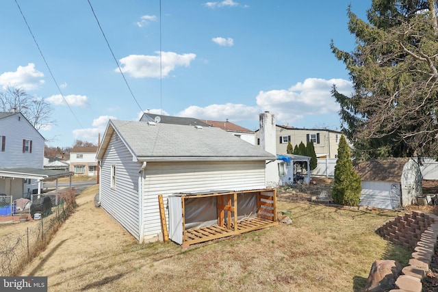back of house featuring fence, a storage shed, roof with shingles, an outdoor structure, and a yard