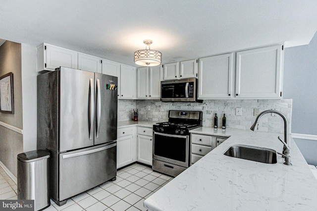 kitchen with light stone countertops, appliances with stainless steel finishes, a sink, baseboards, and decorative backsplash