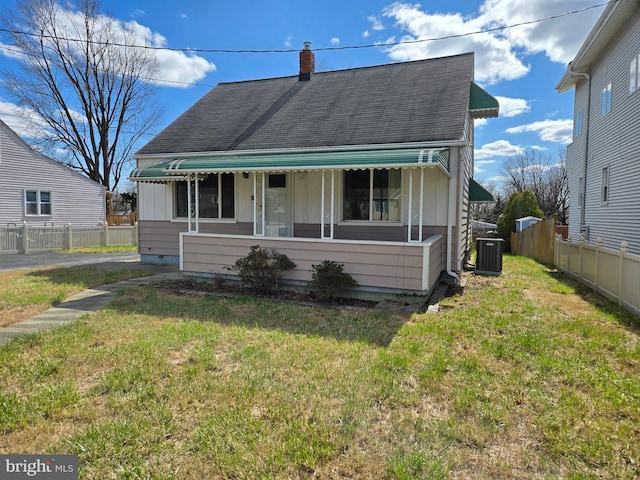 view of front of property featuring fence, central air condition unit, a front yard, roof with shingles, and a chimney