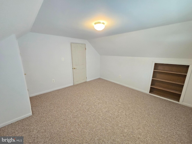 additional living space with baseboards, carpet floors, lofted ceiling, and built in shelves