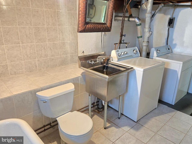 washroom featuring light tile patterned floors, a sink, tile walls, and separate washer and dryer