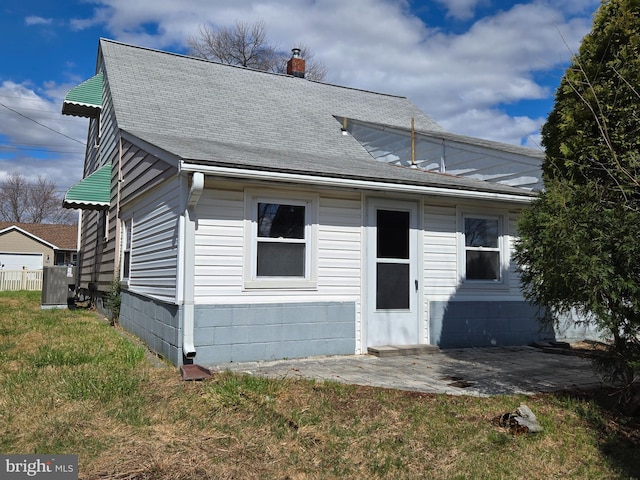 view of front of house with a shingled roof, a front yard, cooling unit, a chimney, and a patio area