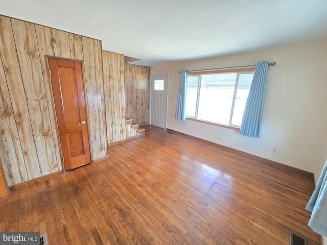 unfurnished living room with visible vents, wood walls, stairs, and wood finished floors