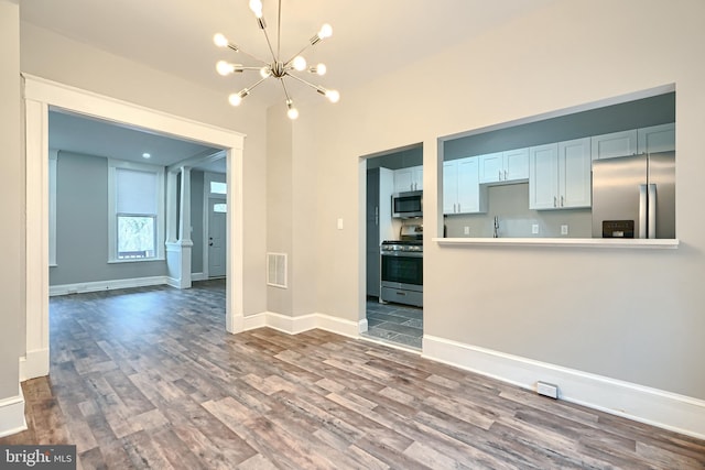 unfurnished living room featuring visible vents, baseboards, an inviting chandelier, wood finished floors, and a sink