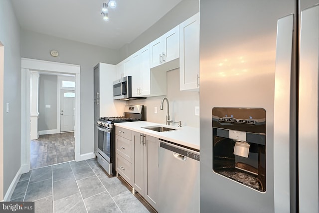 kitchen with baseboards, light countertops, appliances with stainless steel finishes, white cabinetry, and a sink