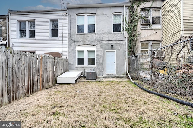rear view of property with central AC unit, stucco siding, a lawn, and a fenced backyard