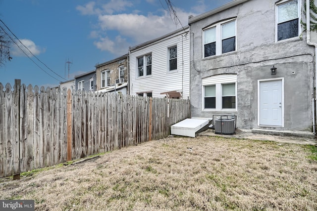 back of property with stucco siding, a lawn, cooling unit, and fence
