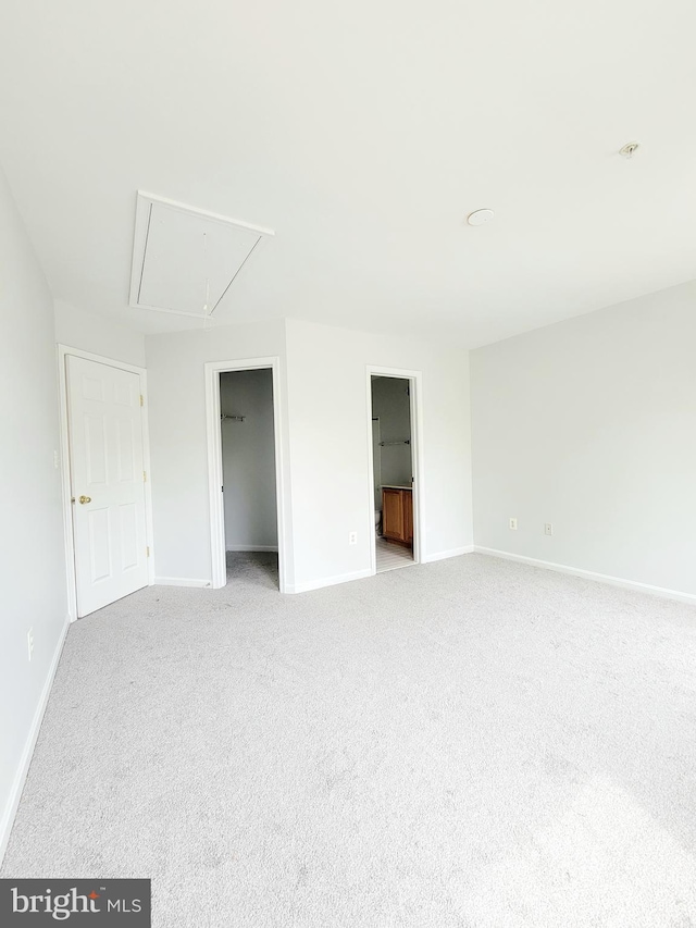 unfurnished bedroom with a walk in closet, attic access, baseboards, carpet floors, and ensuite bath