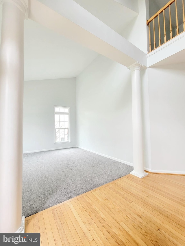 carpeted empty room with hardwood / wood-style floors, high vaulted ceiling, baseboards, and decorative columns
