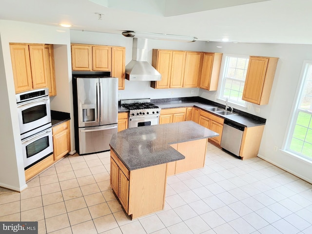 kitchen with stainless steel appliances, light brown cabinets, a sink, wall chimney range hood, and a center island