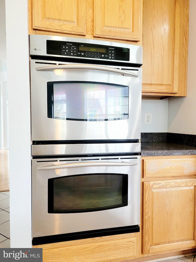 kitchen with double oven, dark countertops, and light brown cabinetry