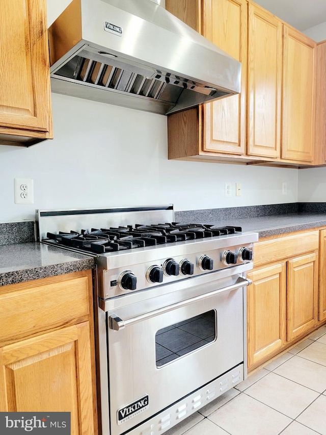 kitchen featuring luxury stove, light brown cabinetry, dark countertops, exhaust hood, and light tile patterned floors