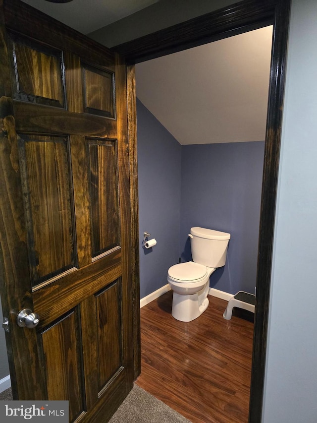 bathroom with lofted ceiling, toilet, wood finished floors, and baseboards