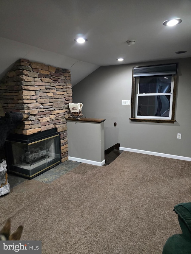 unfurnished living room with carpet, baseboards, lofted ceiling, recessed lighting, and a stone fireplace