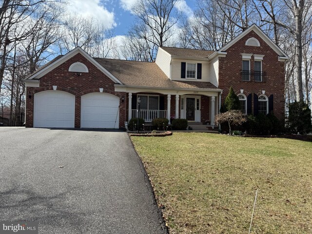 traditional-style home featuring a front yard, brick siding, a garage, and aphalt driveway