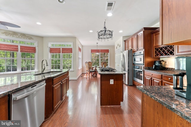 kitchen with dark stone counters, appliances with stainless steel finishes, a sink, a center island, and dark wood-type flooring